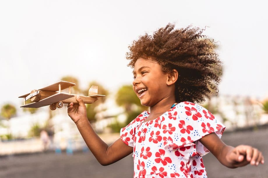 a girl plays with a wooden toy biplane