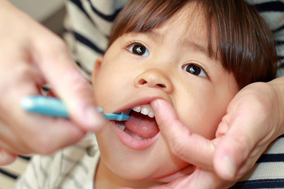 Toddler getting teeth brushed with blue toothbrush by parent