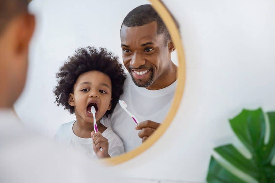 man and son brush teeth in mirror