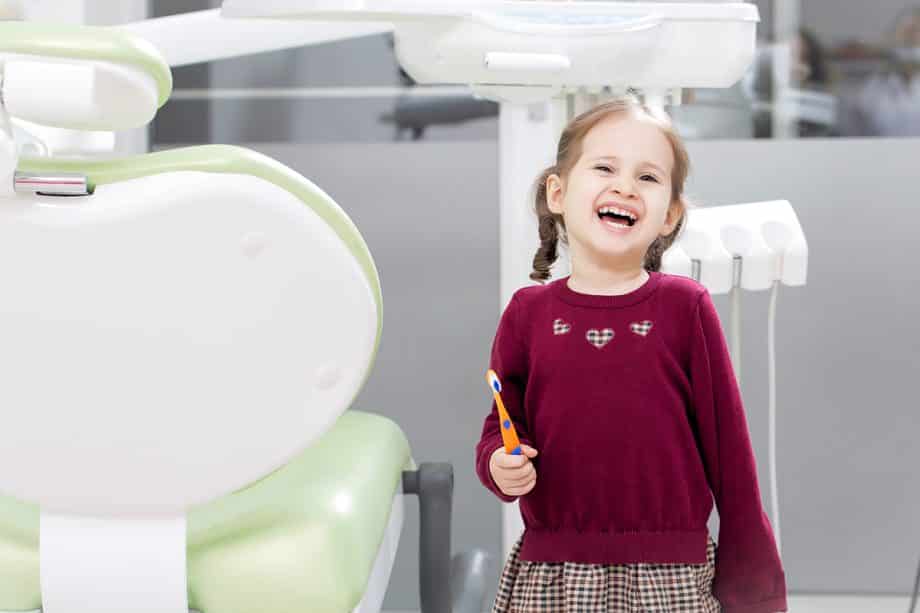 girl laughs while holding toothbrush in dental office