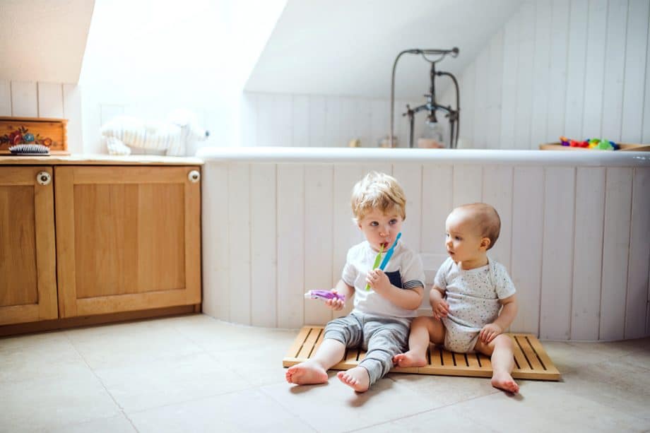 two young boys sit in bathroom with toothbrushes